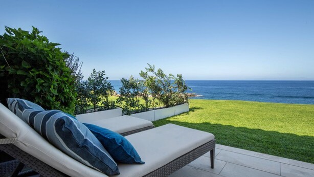 Un patio con dos sillones, un área verde y vista al océano.