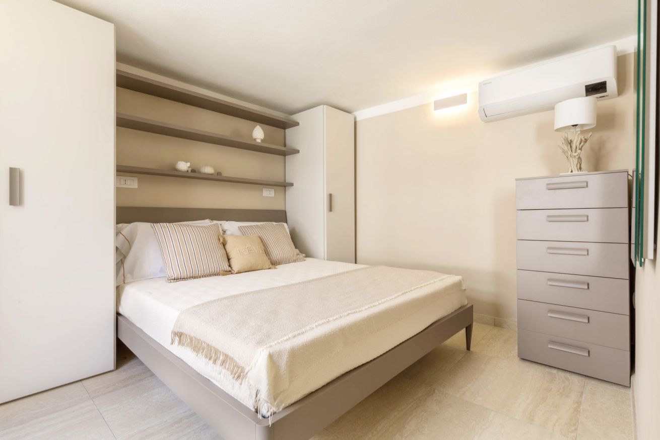 A bedroom with a bed, a dresser, and a wall-mounted air conditioner.