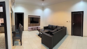 A modern living room with a dark sofa, a coffee table, and a flat-screen TV mounted on the wall.