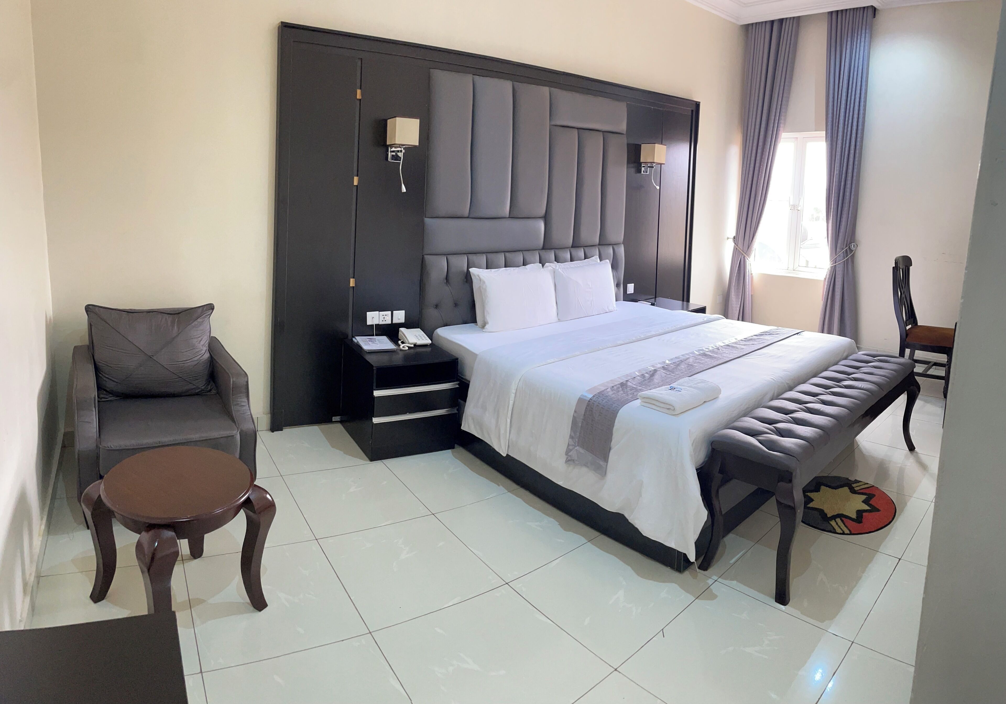 A hotel room with a large bed, a bedside table, a chair, and a small round table.