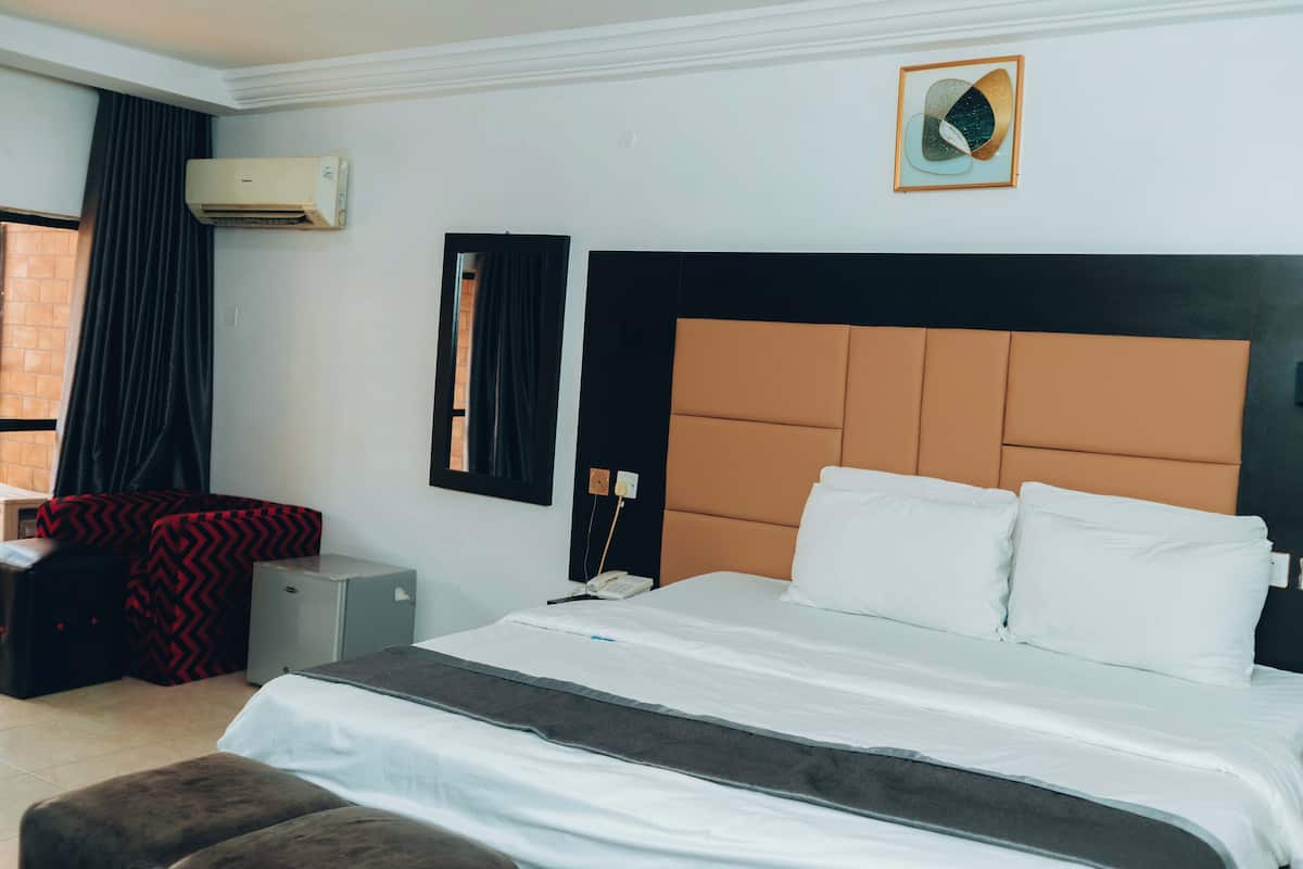 Une chambre d’hôtel avec un grand lit, un bureau, une chaise, un climatiseur et un miroir fixé au mur.
