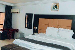 A hotel room with a large bed, a desk, a chair, an air conditioner, and a wall-mounted mirror.