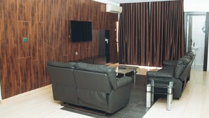 A modern living room with a sectional sofa, a small table, and a flat-screen TV mounted on the wall.