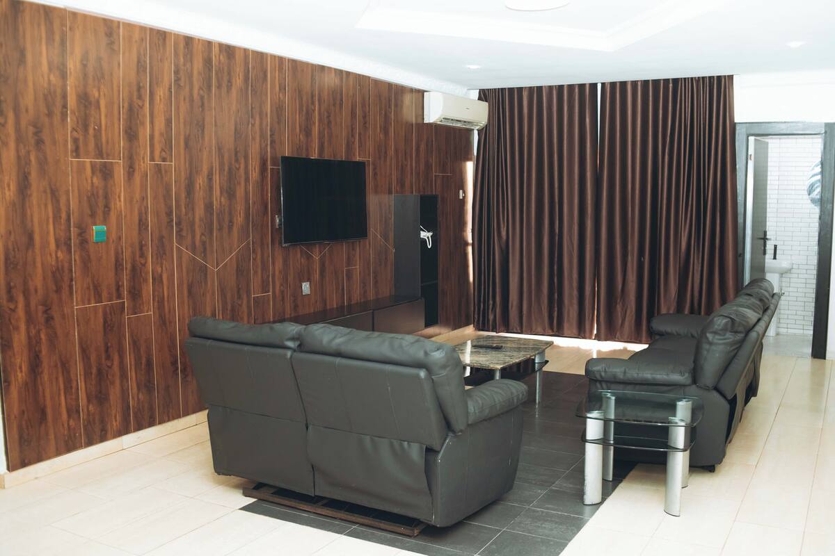 Un salon moderne avec un canapé d’angle, une petite table et un téléviseur à écran plat fixé au mur.