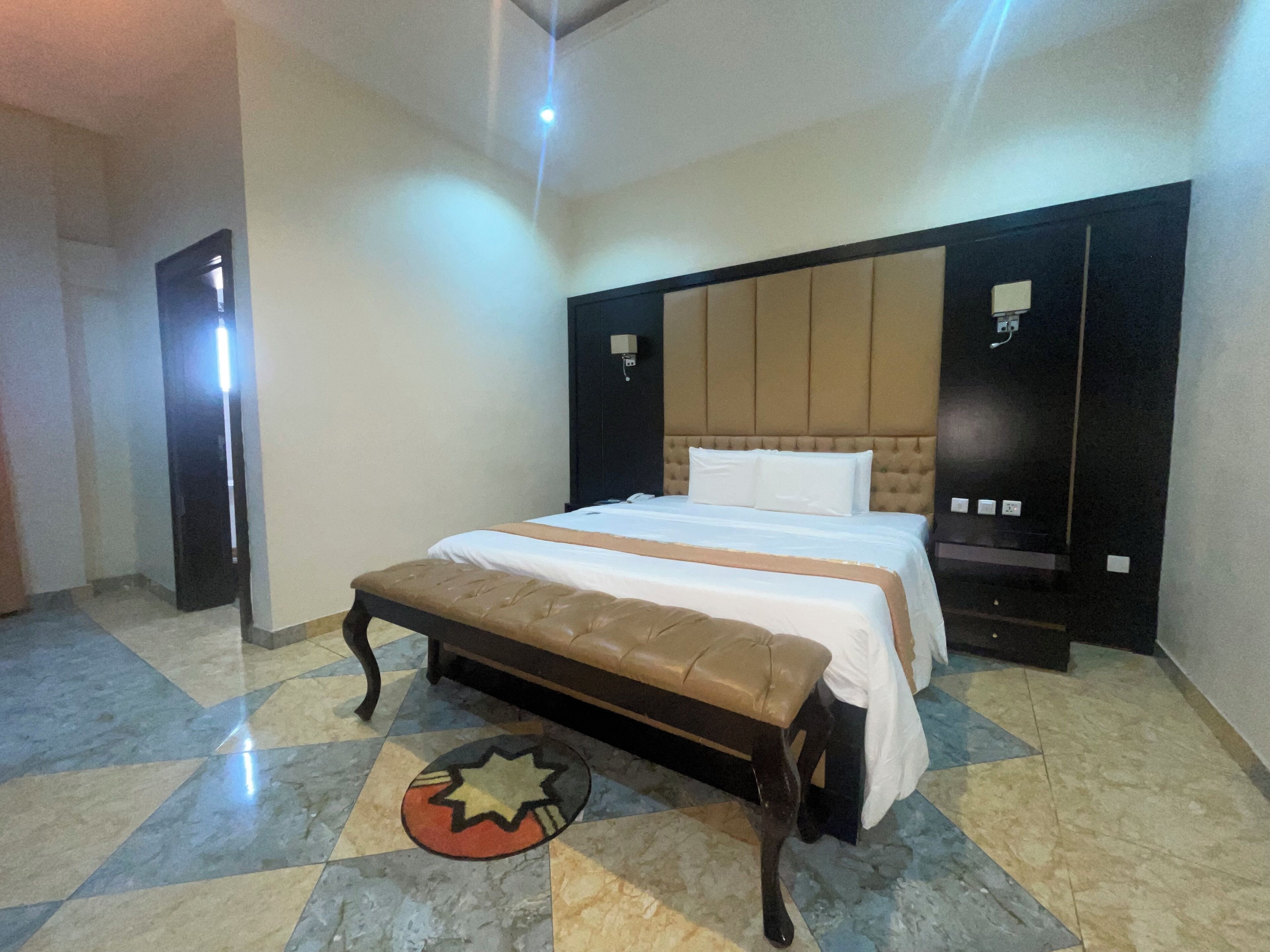 Een hotelkamer met een groot bed, een bankje, een hoofdeinde en een betegelde vloer.
