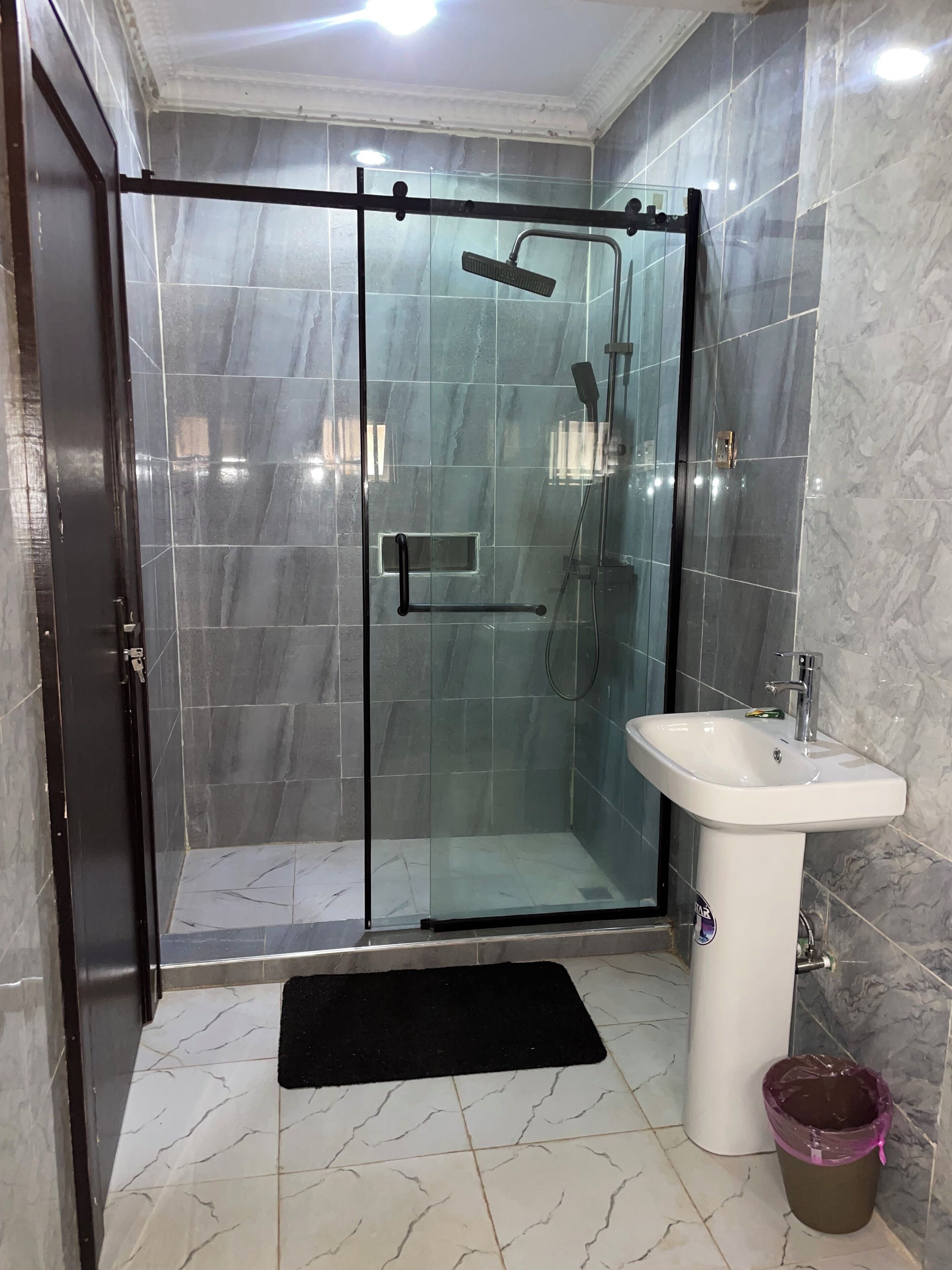 Une salle de bain moderne avec une douche à parois de verre, un lavabo blanc et des carreaux de marbre.