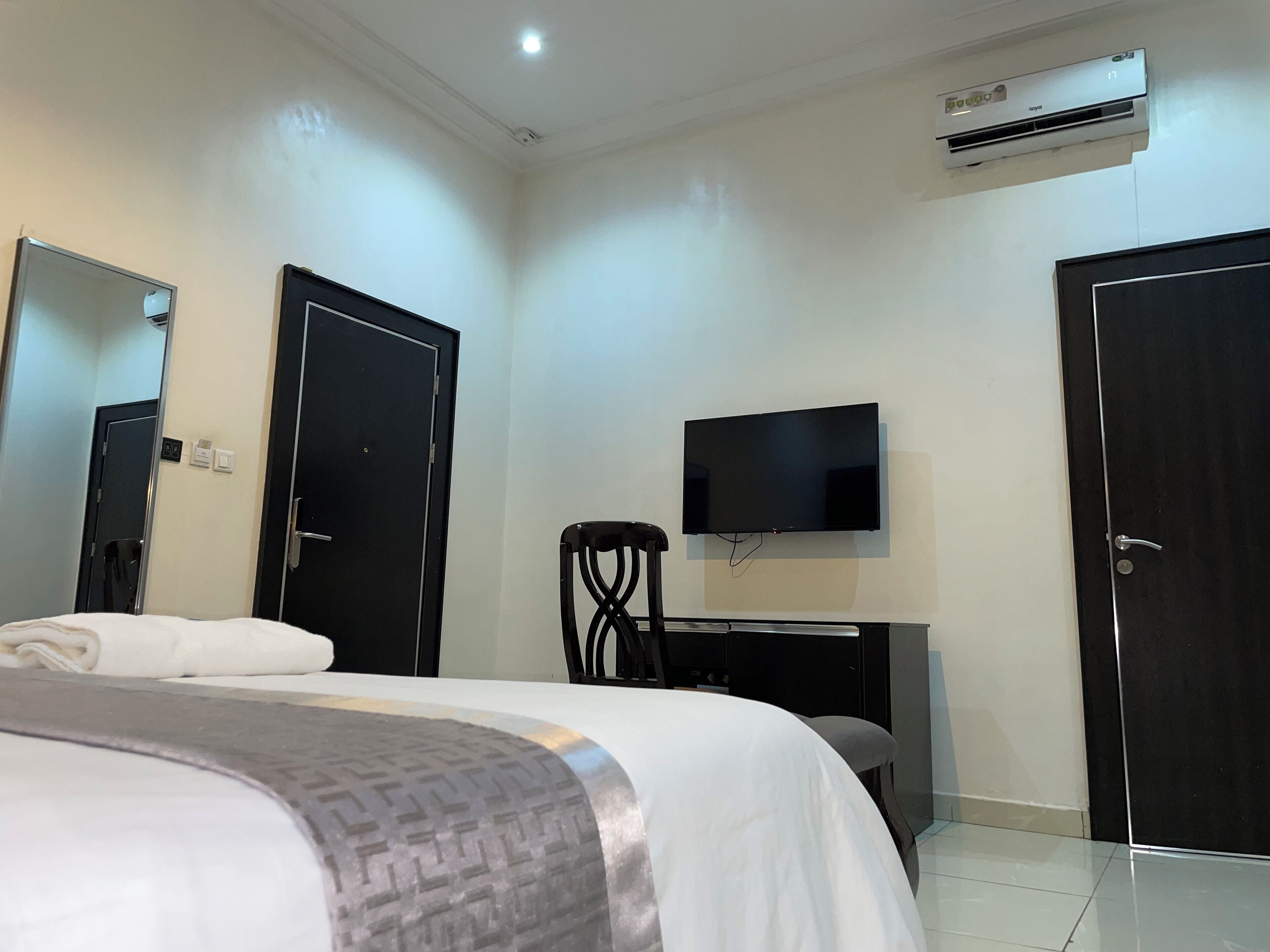 Quarto de hotel com cama, escrivaninha, cadeira, televisão e duas portas.