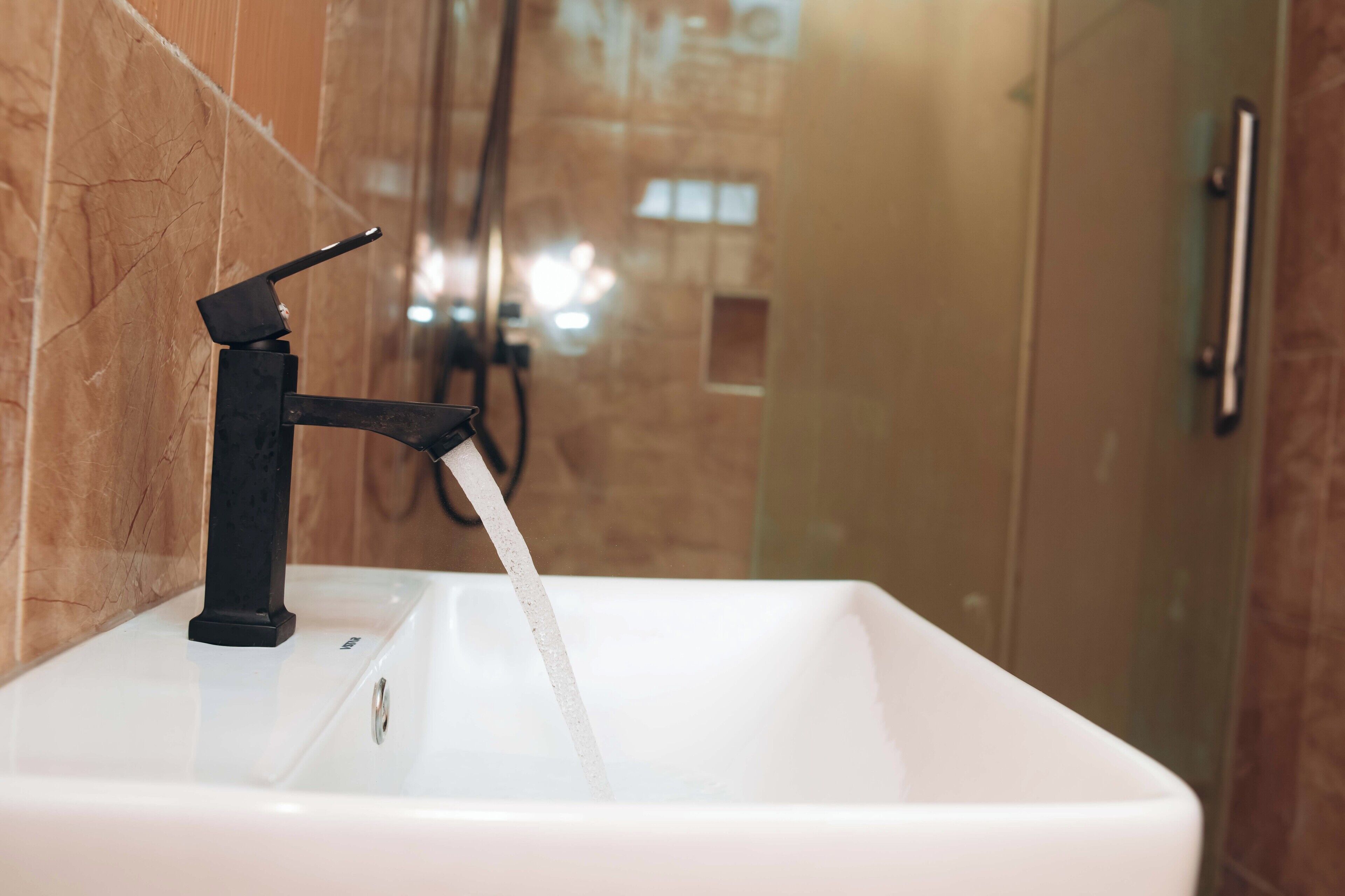Un bagno con un lavandino bianco, un rubinetto nero e un box doccia in vetro.