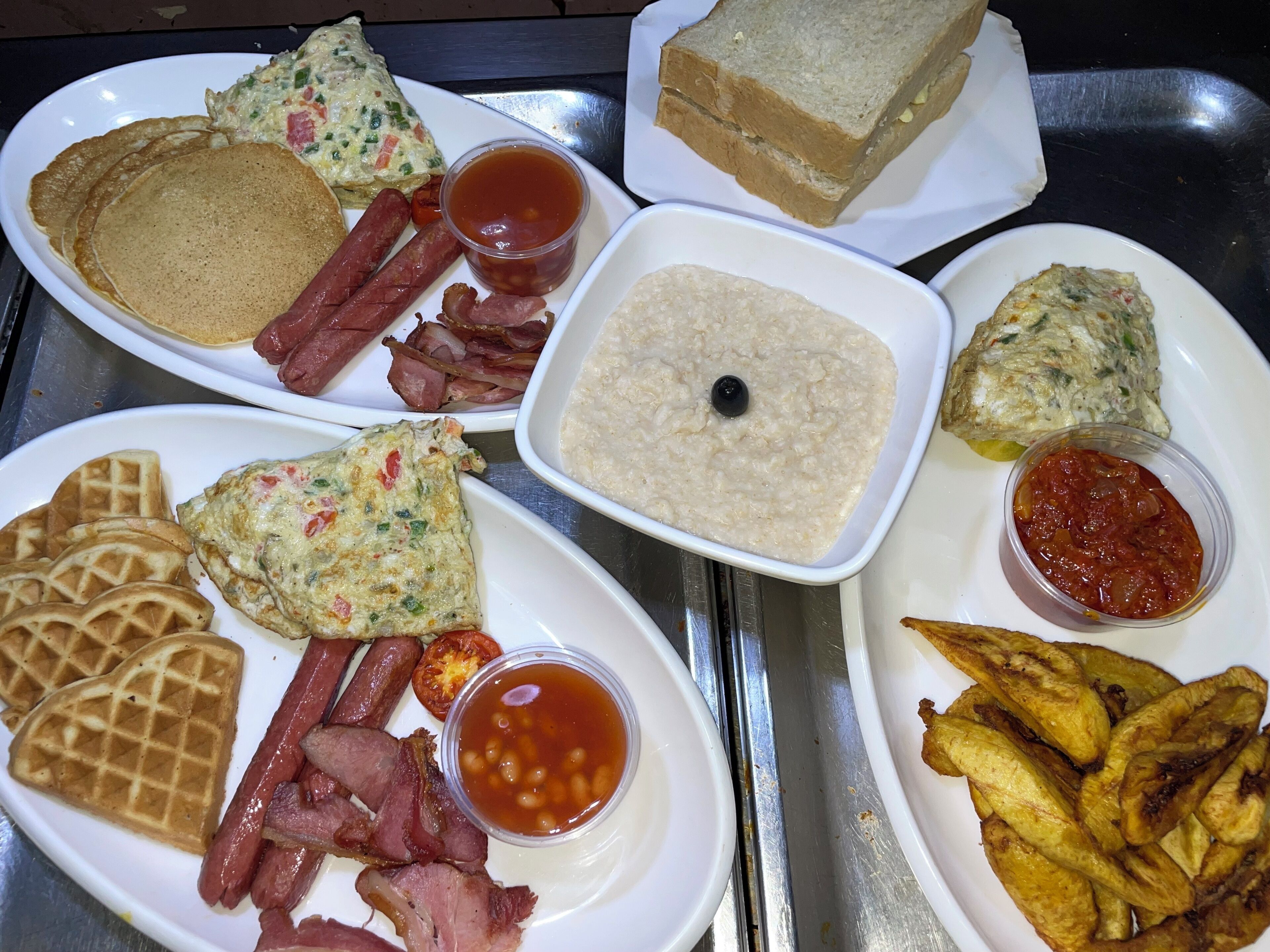 A breakfast tray with pancakes, bacon, waffles, omelettes, toast, and various dips.