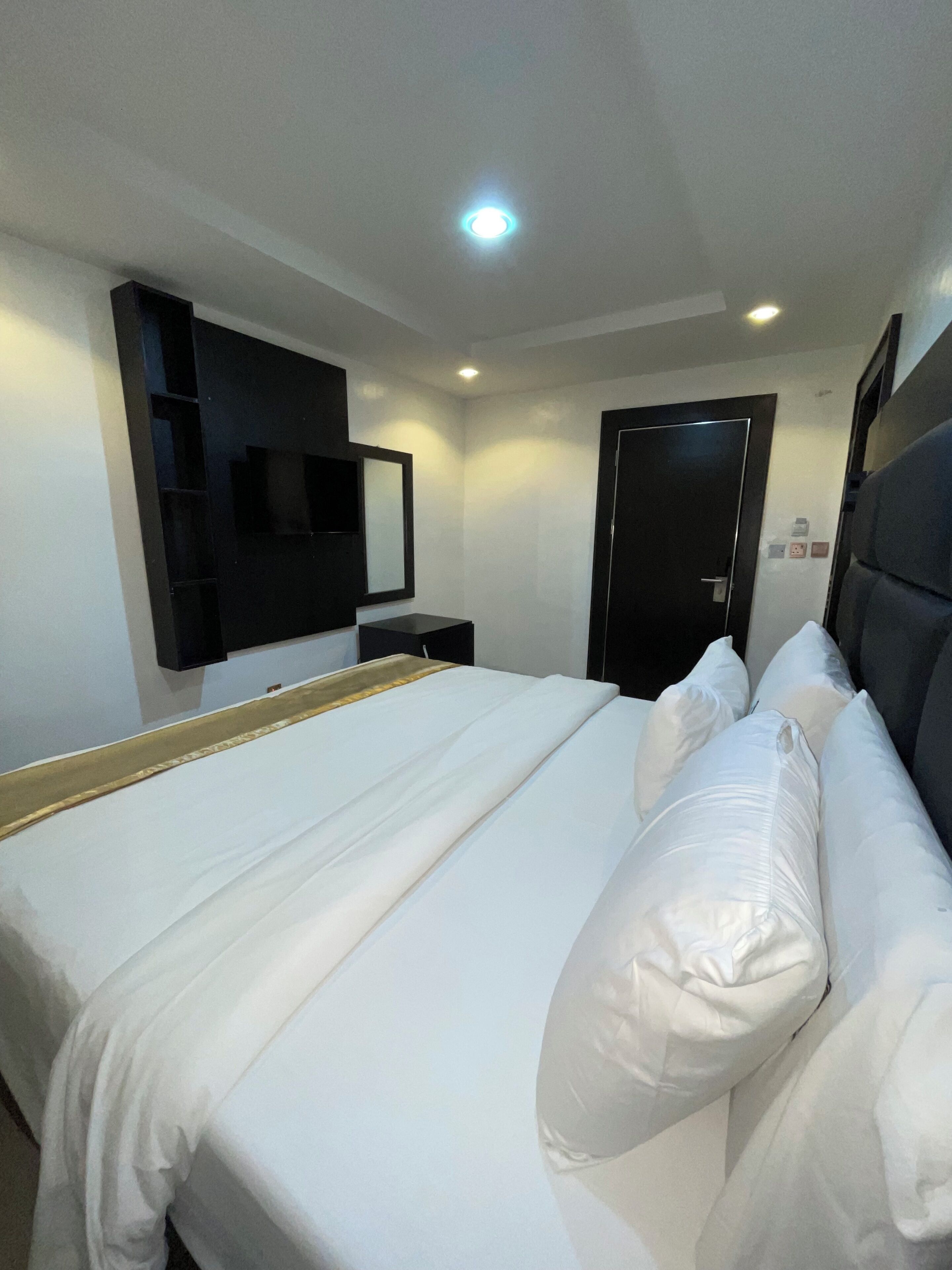 A hotel room with a large bed, a bedside table, a mirror, and a door.