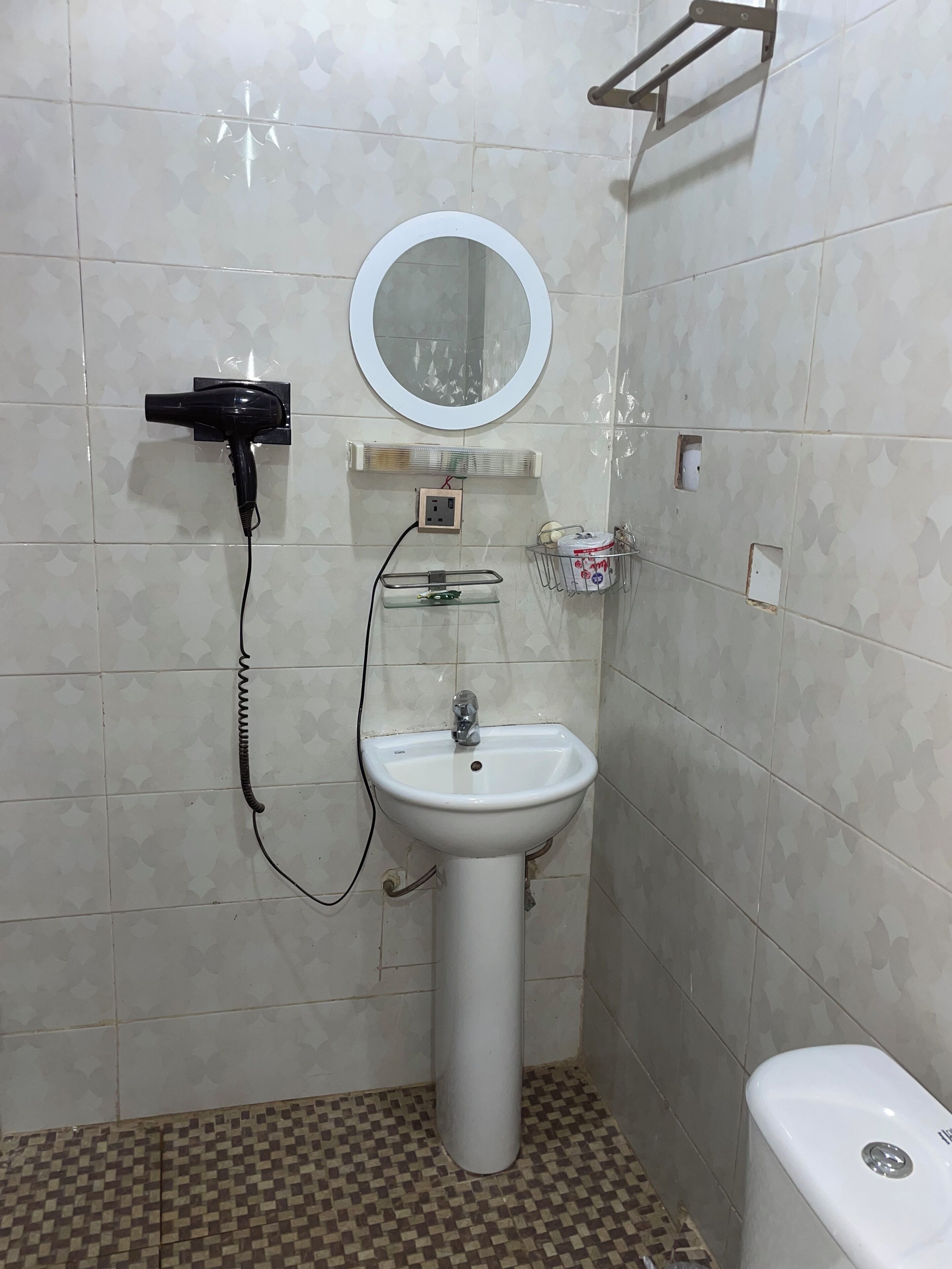 Et badeværelse med et hvidt pedikurvask, et spejl over vasken, en hårtørrer og en lille hylde med toiletartikler.