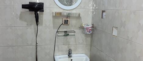 Ein Badezimmer mit einem weißen Waschbecken auf Säule, einem Spiegel darüber, einem Haartrockner und einer kleinen Ablage mit Pflegeprodukten.