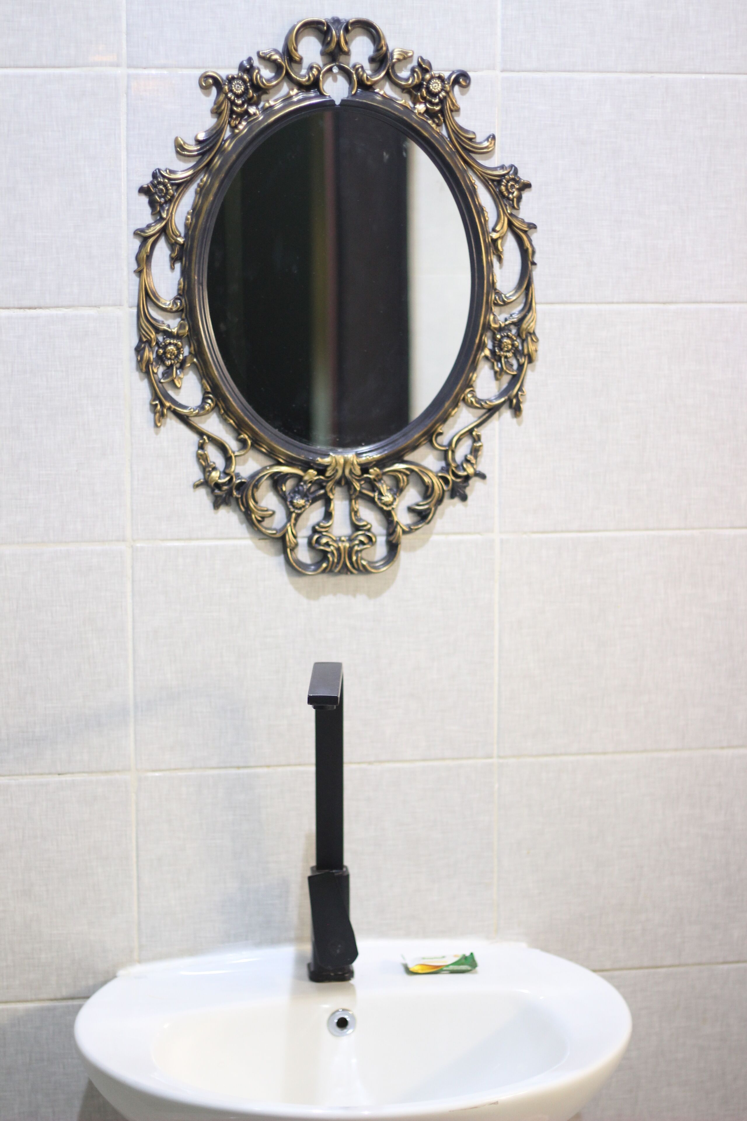 A bathroom with a white sink, a black faucet, and an ornate gold-framed mirror.