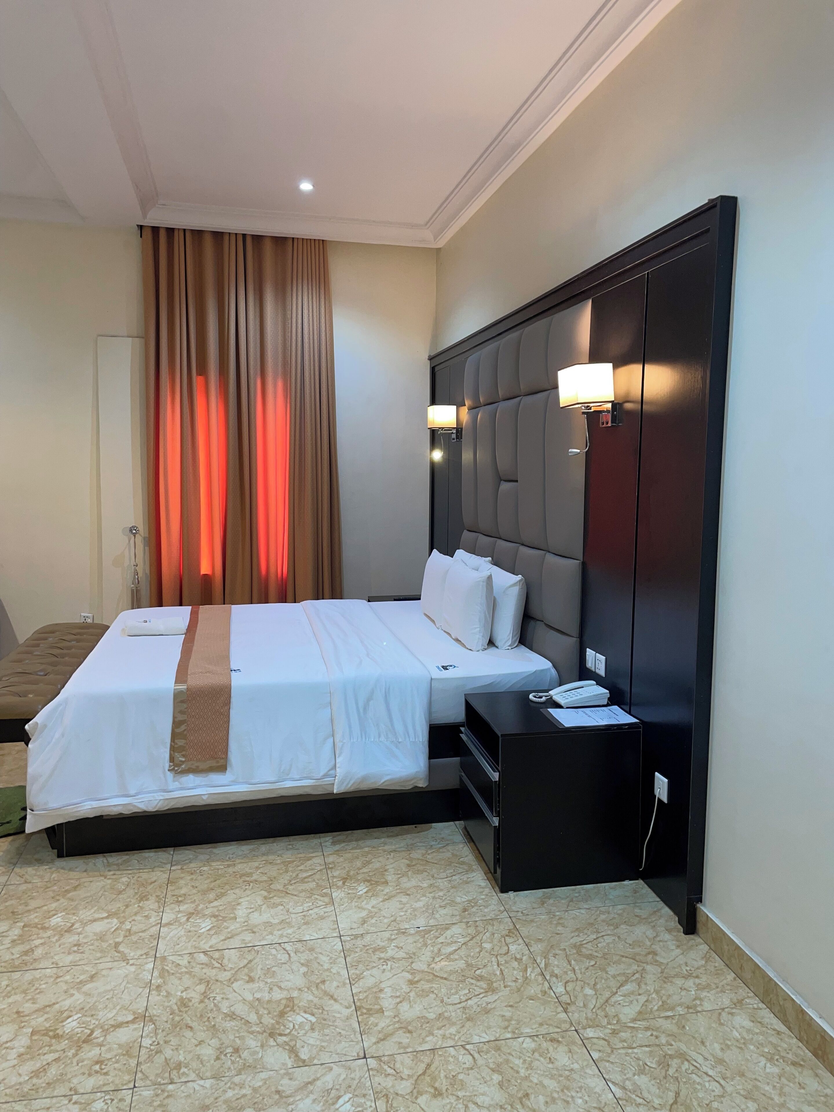 A hotel room with a large bed, a bedside table, a lamp, and a wardrobe.