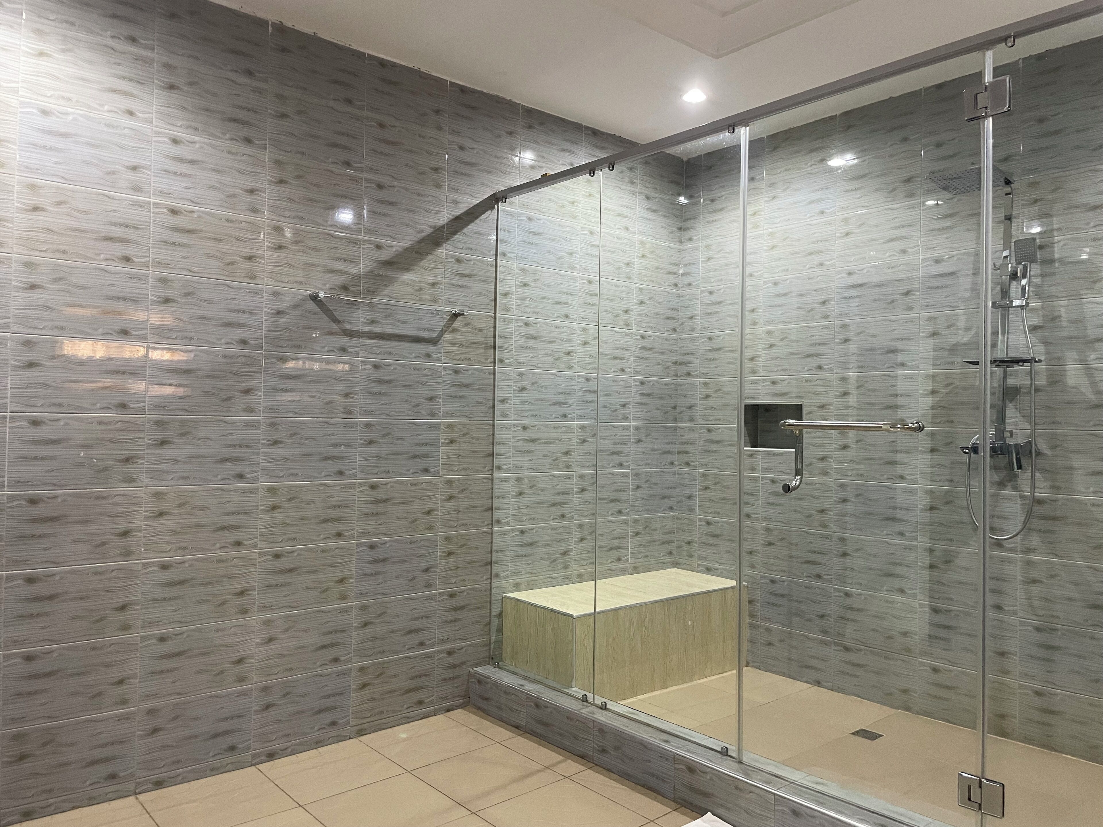 A modern shower with a glass enclosure, a wooden bench, and a wall with a wood grain pattern.