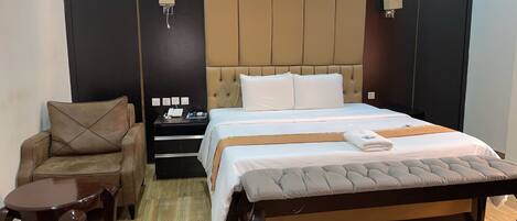 A hotel room with a large bed, a chair, a nightstand, and a small table.