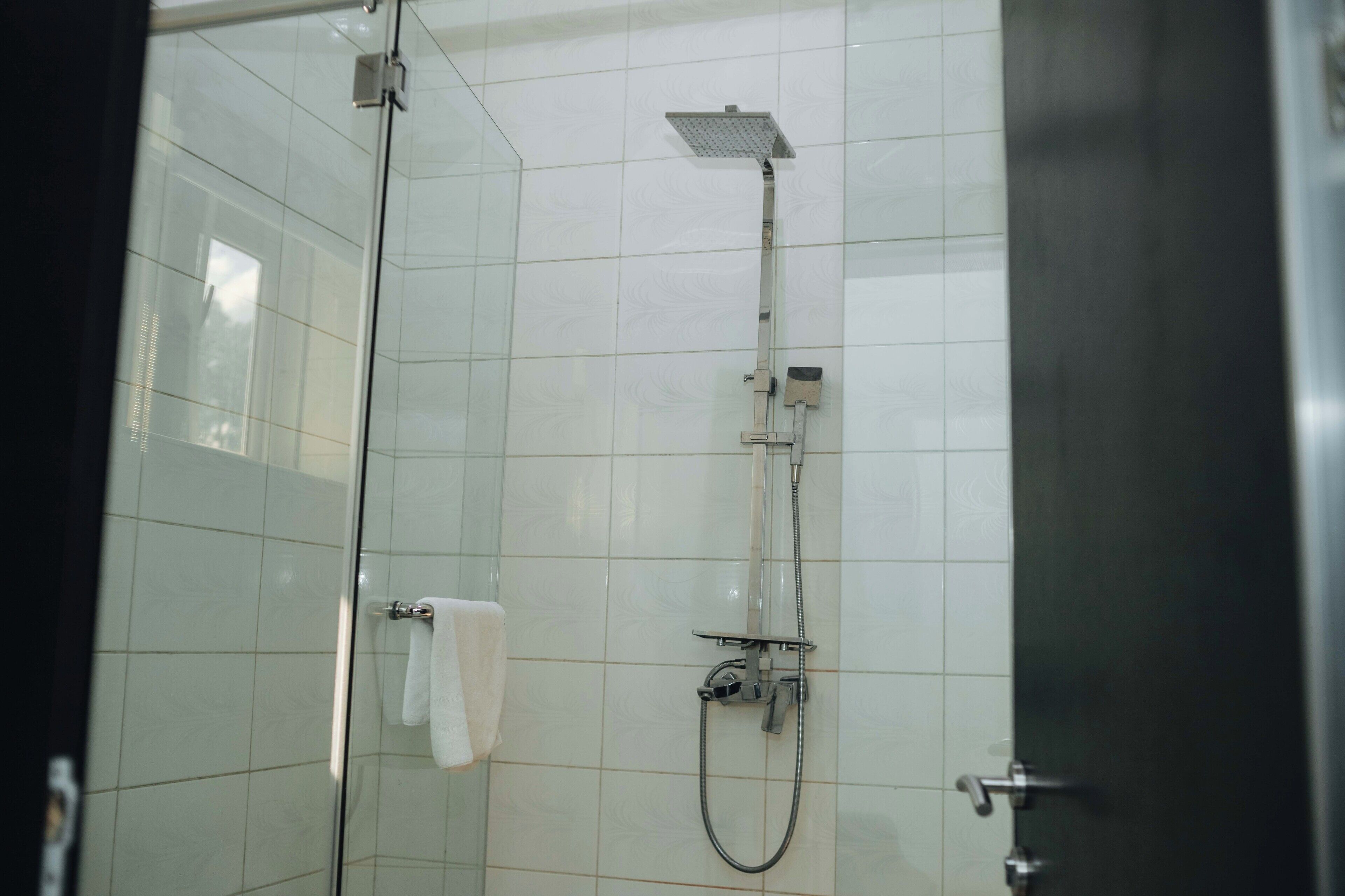 A glass-enclosed shower with a handheld showerhead and a fixed overhead showerhead.