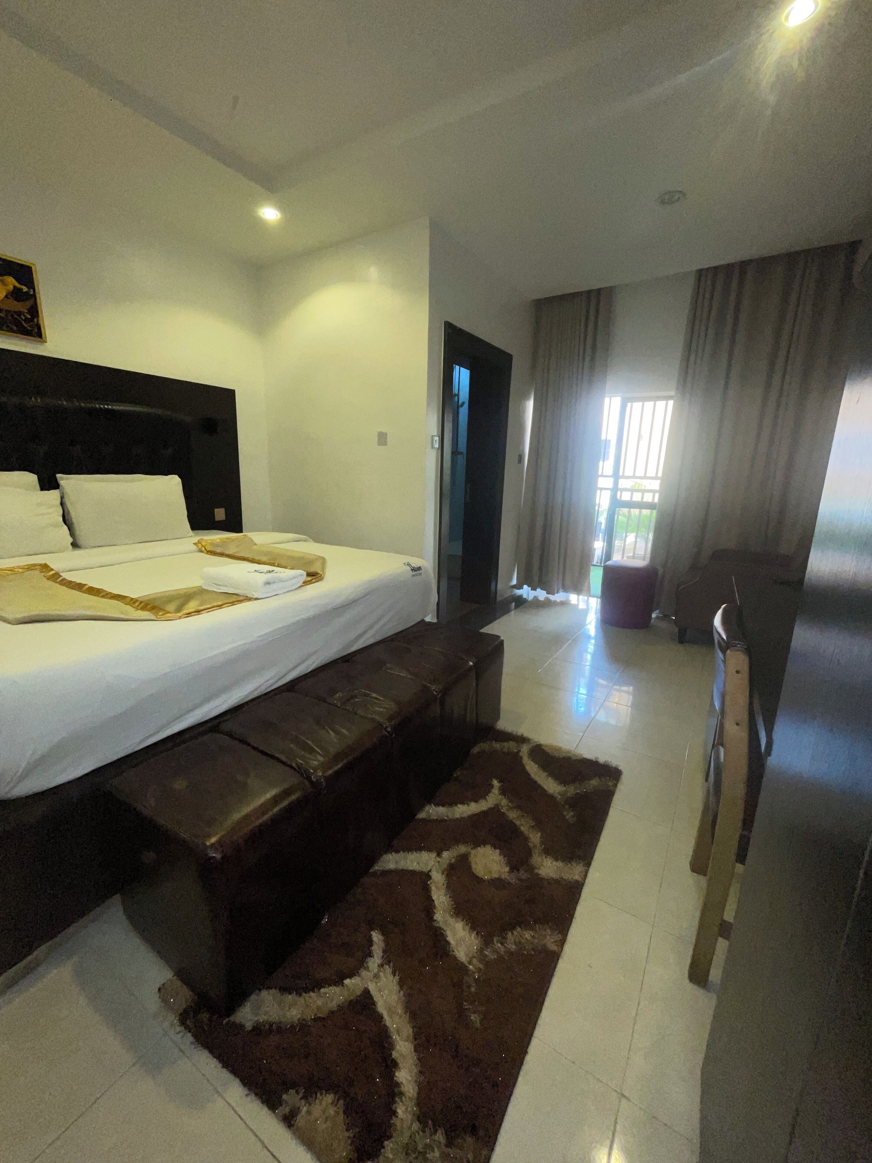 A hotel room with a large bed, a bench, a desk, and a view of the outdoors.