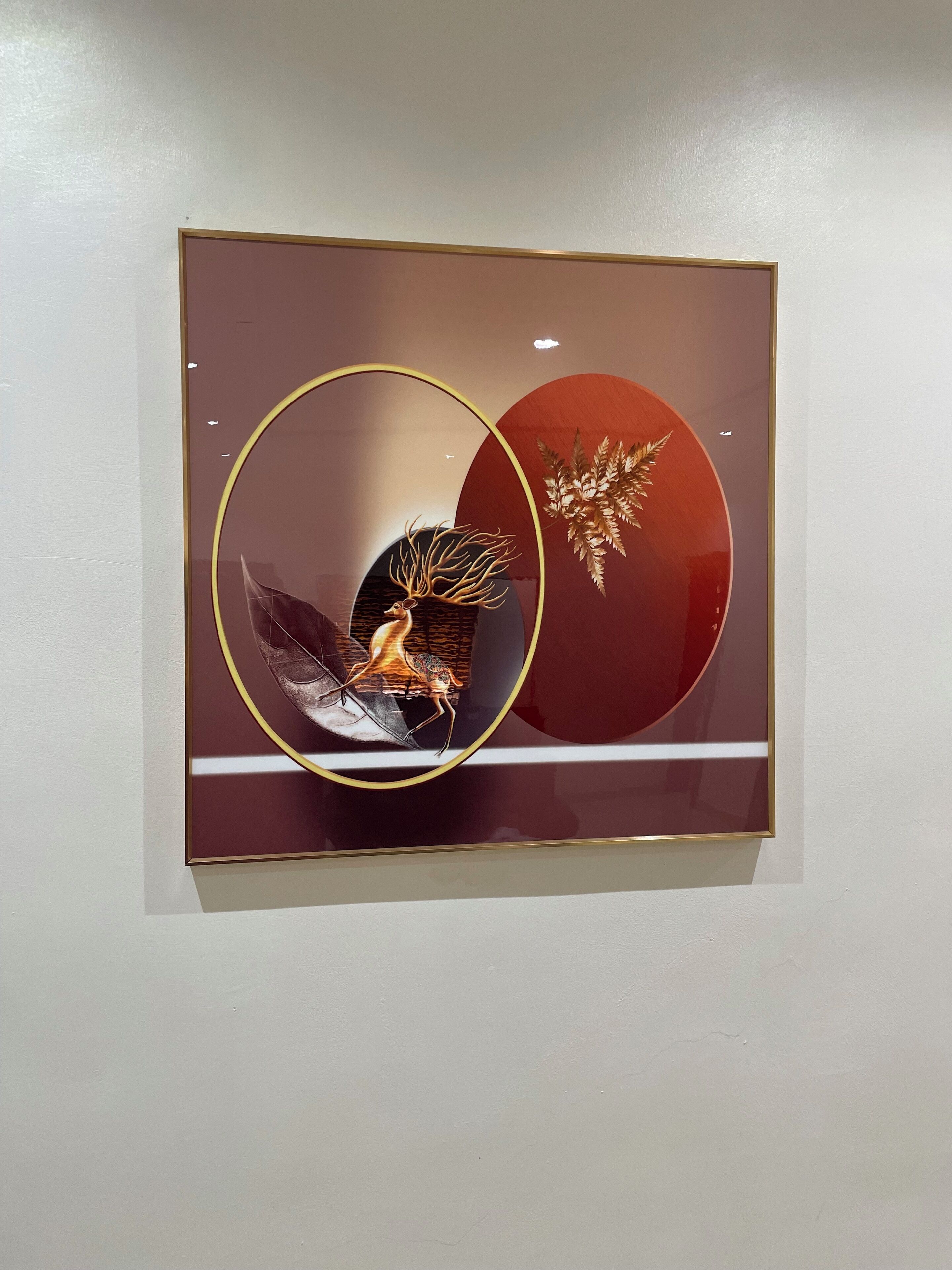 Een lijst met een kunstwerk, waarop een ontwerp van een hert en varens te zien is, hangt aan een muur.