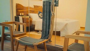 Ένα δωμάτιο ξενοδοχείου με ένα κρεβάτι, δύο ξύλινες καρέκλες, έναν καθρέφτη και μια κουρτίνα.