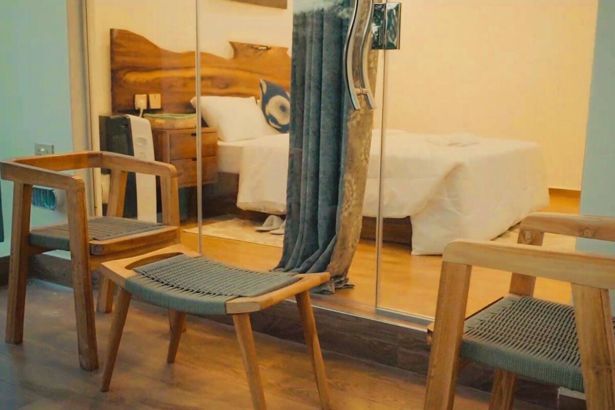 Habitación de hotel con cama, dos sillas de madera, un espejo y una cortina.