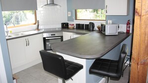 A modern kitchen with white cabinets, a black countertop, and a built-in stove. There are two black bar stools and a window providing natural light.