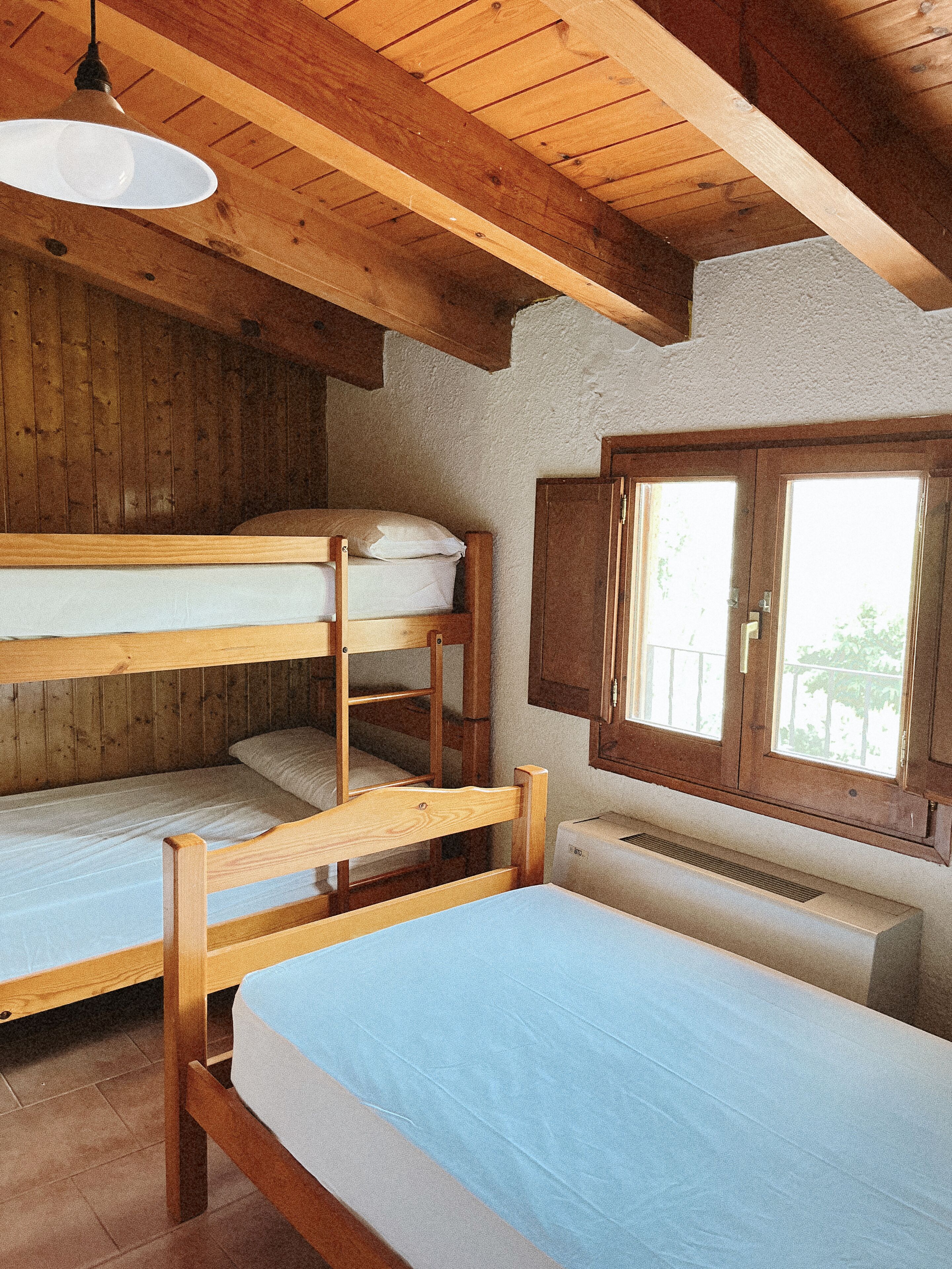 Una habitación con literas, vigas de madera, un ventanal y un radiador.