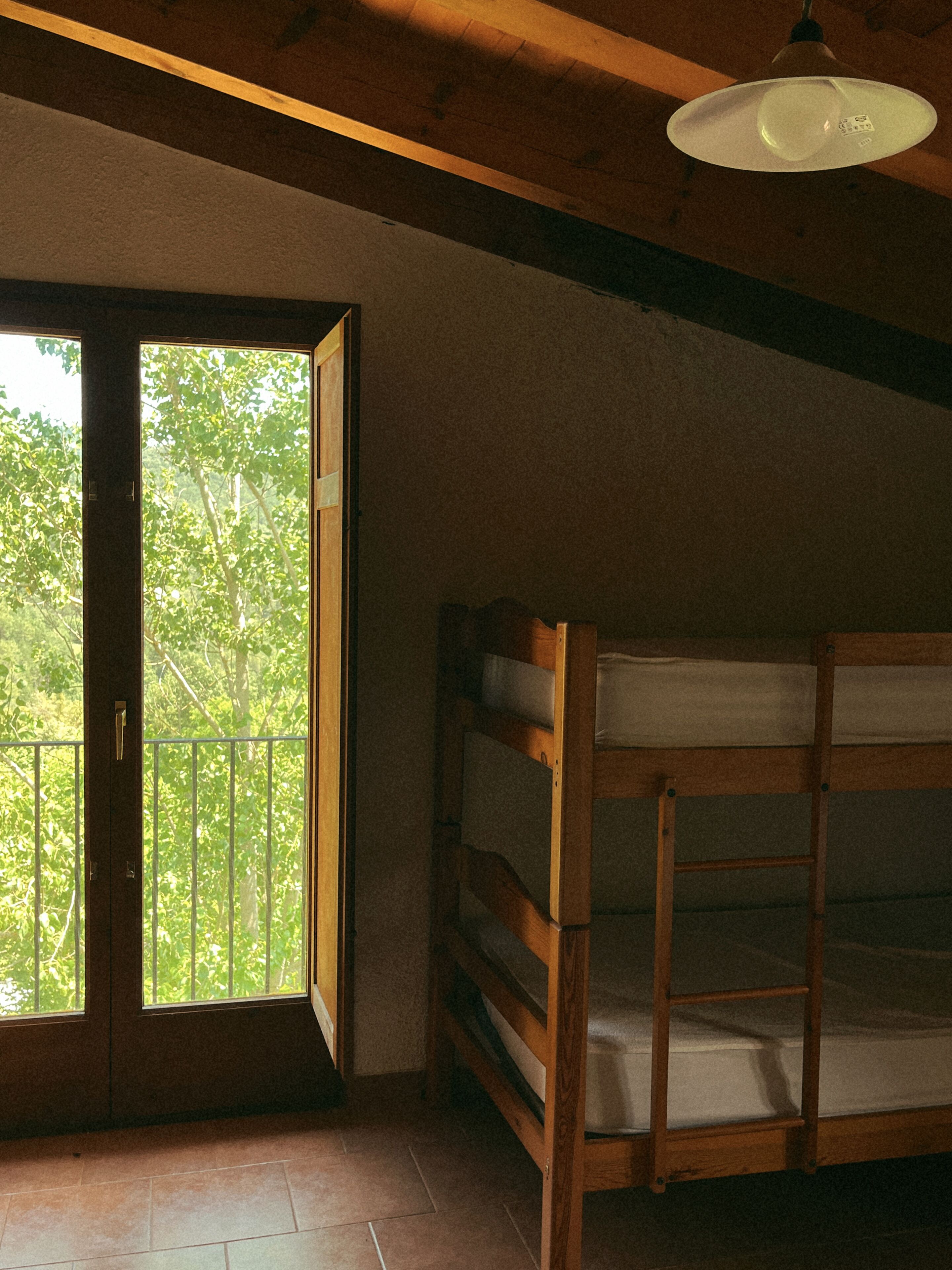 Una habitación con una cama nido de madera, un ventanal con vistas a árboles y una lámpara en el techo.