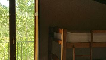 Una habitación con una cama nido de madera, un ventanal con vistas a árboles y una lámpara en el techo.