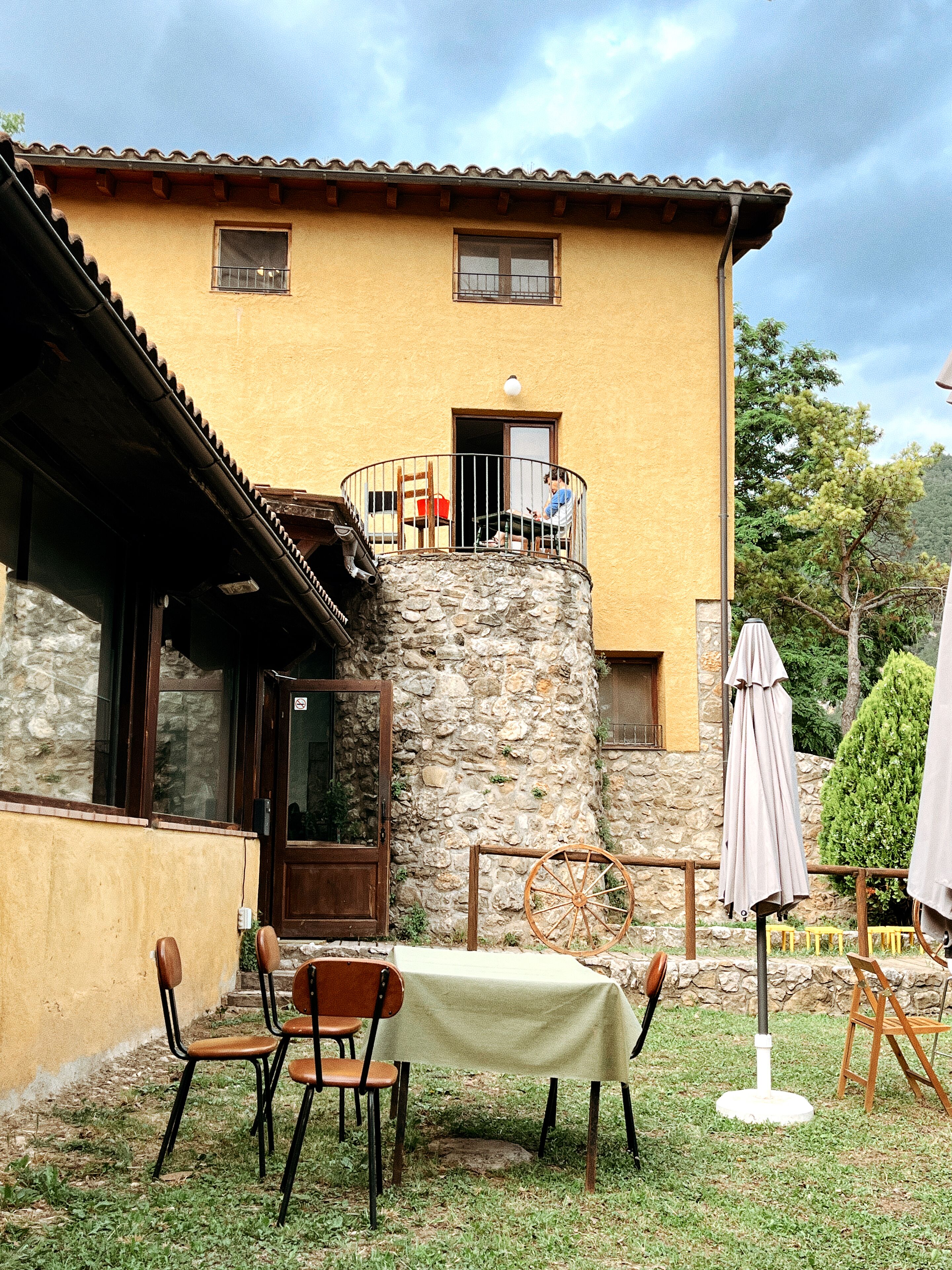 A stone house with a balcony, a table with chairs, and two umbrellas.