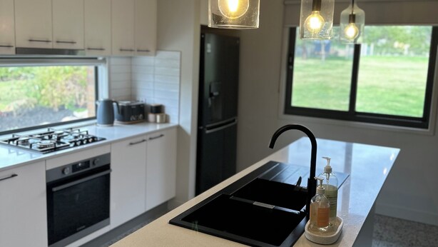 Une cuisine moderne dotée d’un îlot central, d’appareils électroménagers en acier inoxydable et de luminaires suspendus.