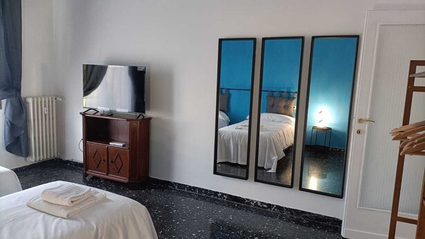 Habitación de hotel con una cama, un armario de madera, un televisor y tres espejos en la pared.