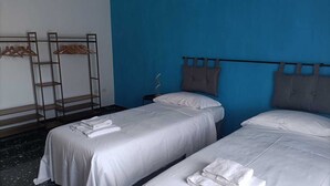 Habitación de hotel con dos camas, una pared azul y un armario de madera con ropa colgada.