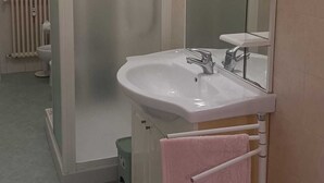 Un baño con lavamanos blanco, espejo y cabina de ducha.