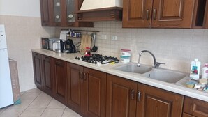 Una cocina con armarios de madera, una encimera blanca, una estufa, un fregadero y diversos electrodomésticos.