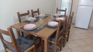 Una mesa de comedor dispuesta con platos rosas y vasos transparentes, rodeada de sillas de madera con asientos acolchados.