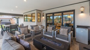 Un salon moderne doté d’une cheminée, de sièges confortables et d’un coin cuisine visible à travers des portes vitrées.