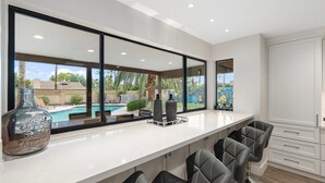 Une cuisine moderne dotée d’une grande fenêtre donnant sur une piscine et un jardin.
