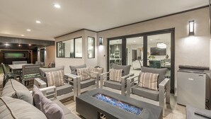 Un salon moderne avec une cheminée, des canapés gris et un coin repas comprenant une table et des chaises.