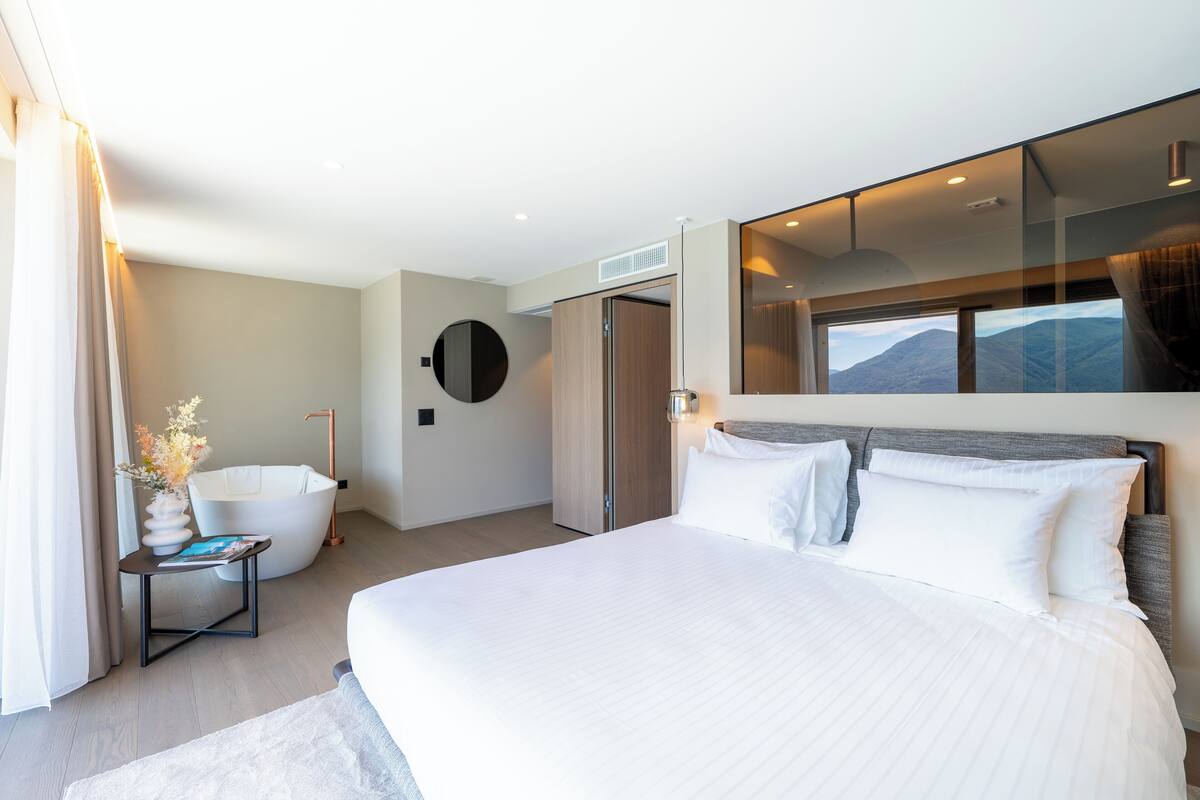 Een moderne hotelkamer met een groot bed, een badkuip en uitzicht op bergen.