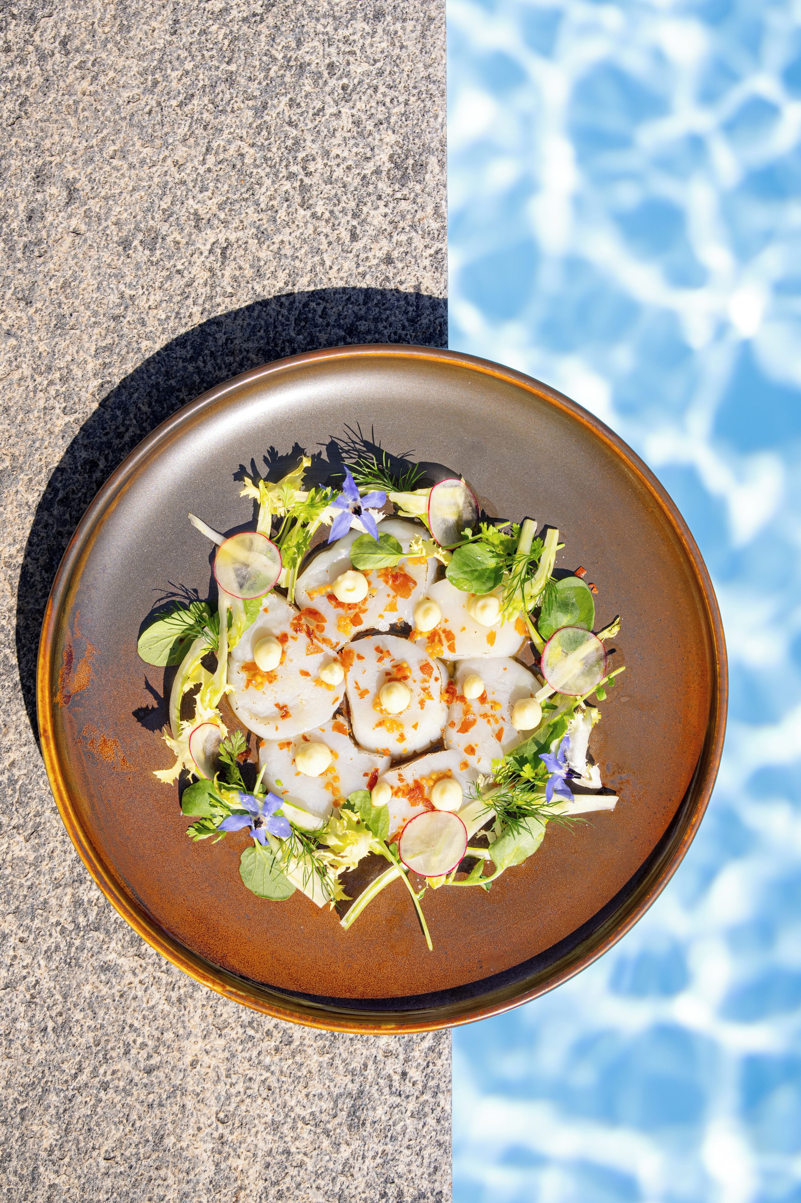 Une assiette remplie de différents légumes et accompagnée d’une sauce, posée sur une table à côté d’une piscine.