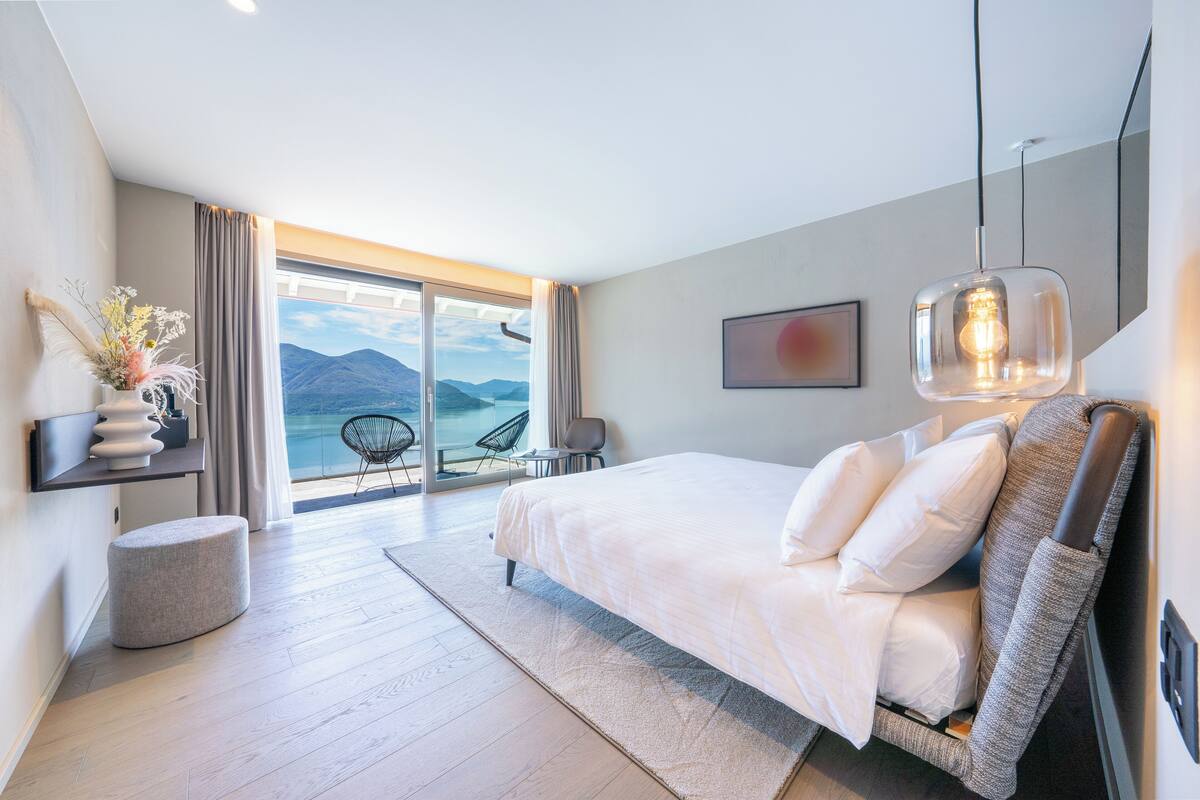 Een moderne slaapkamer met een groot bed, uitzicht op bergen en een balkon met stoelen.