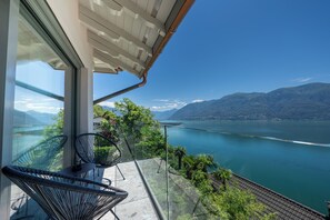 A balcony with glass railings overlooking a lake and mountains. - Boutique Hotel Elisabetta (Ronco sopra Ascona)