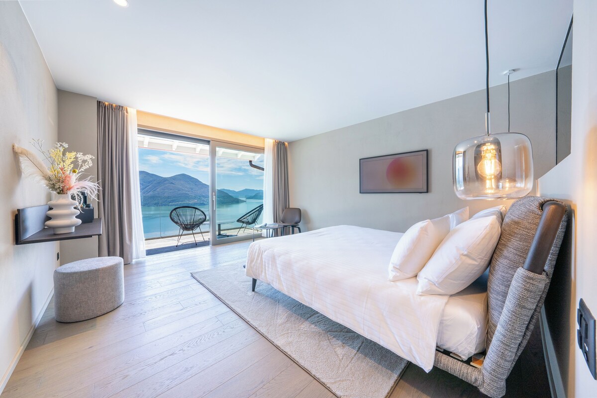 Una camera da letto moderna con un letto grande, vista sulle montagne e un balcone con sedie.