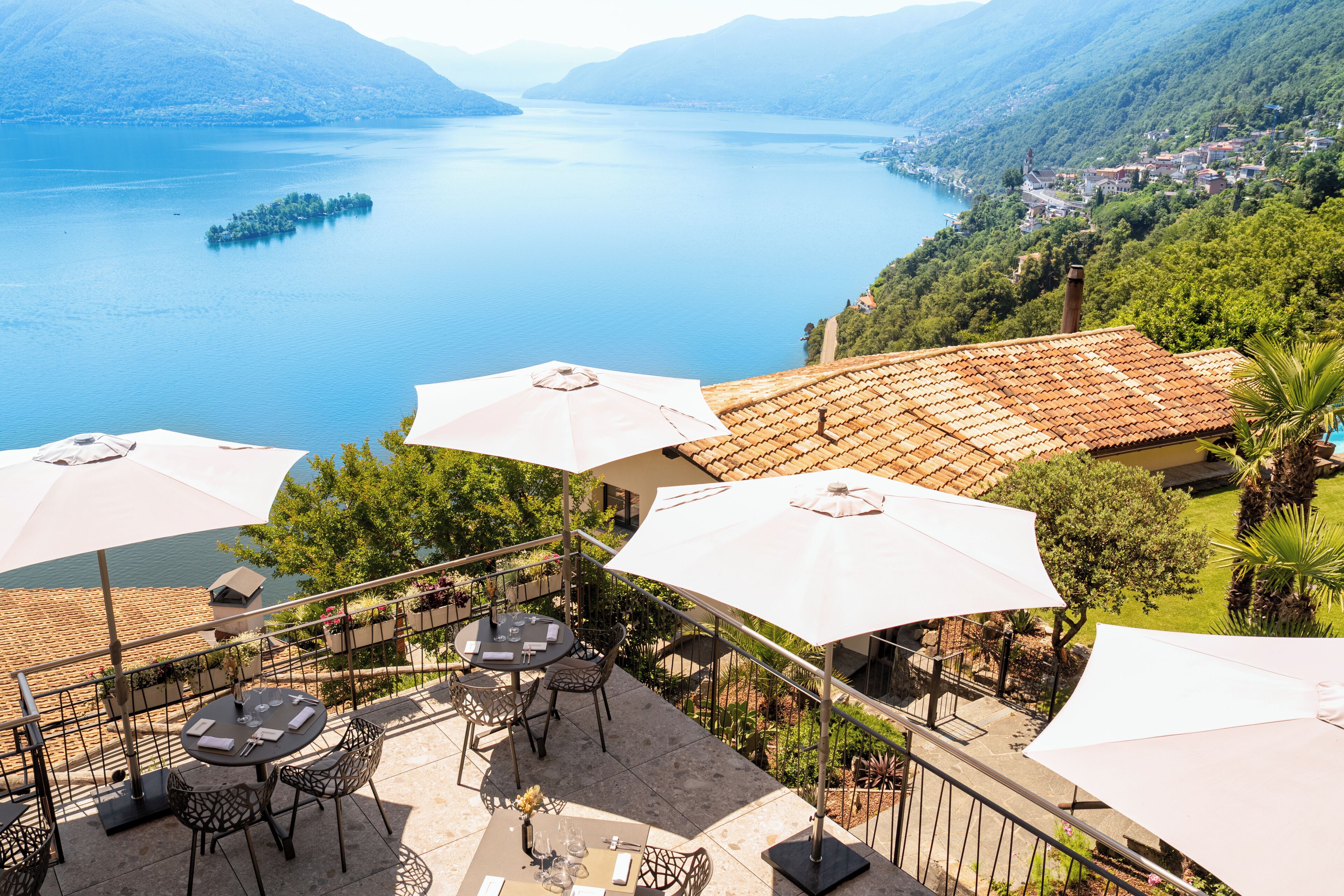 Une terrasse extérieure avec des tables et des parasols, offrant une vue sur un lac et des montagnes.