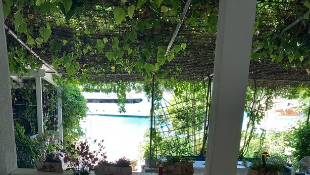 A covered outdoor seating area with a view of a pool and a white building in the background. - Guest House Green Corner Supetarska Draga (Rab)