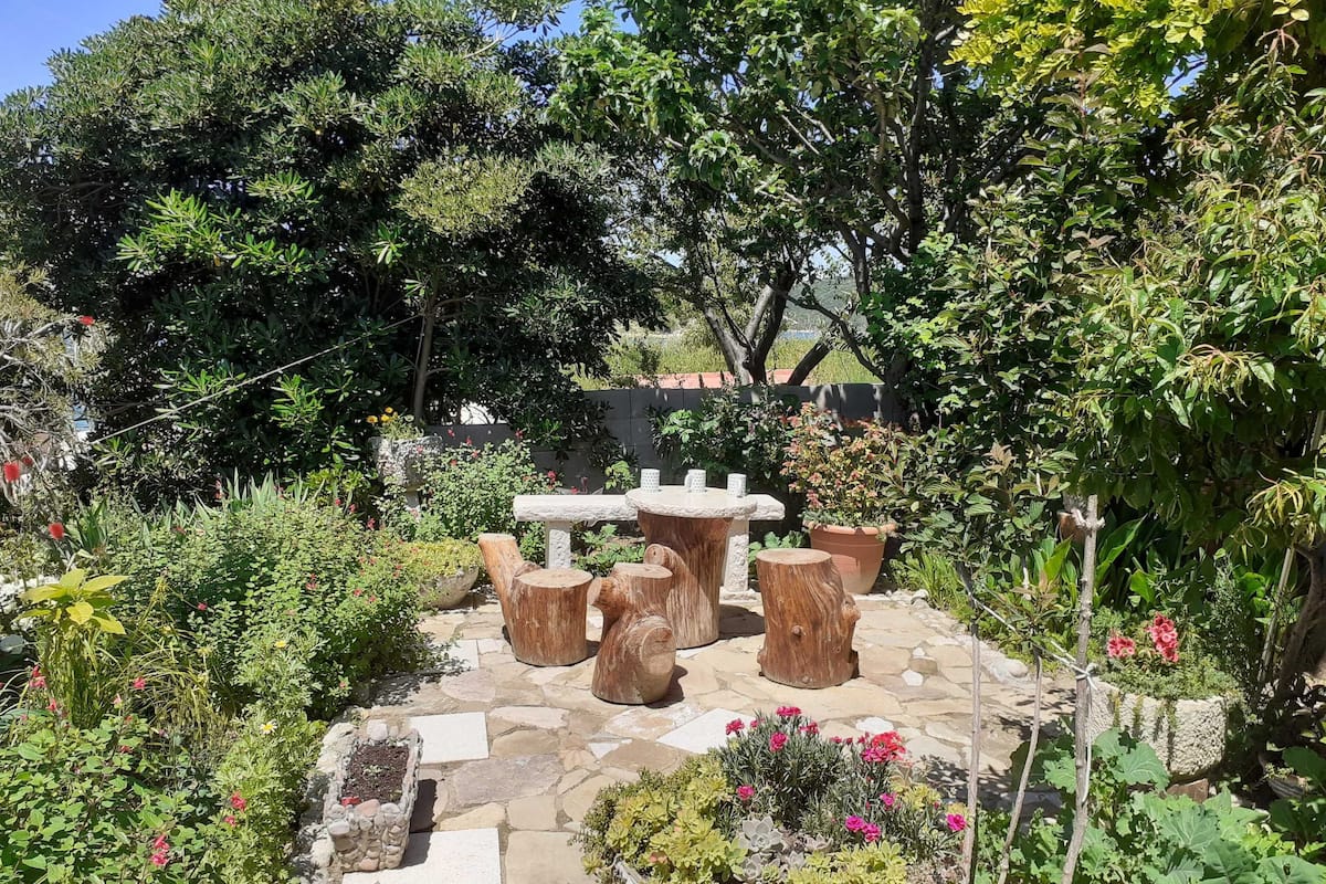 A garden patio with stone flooring, rustic wooden stools, and a stone table.
