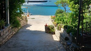 A pathway leading to a marina with a yacht docked in the background. - Guest House Green Corner Supetarska Draga (Rab)