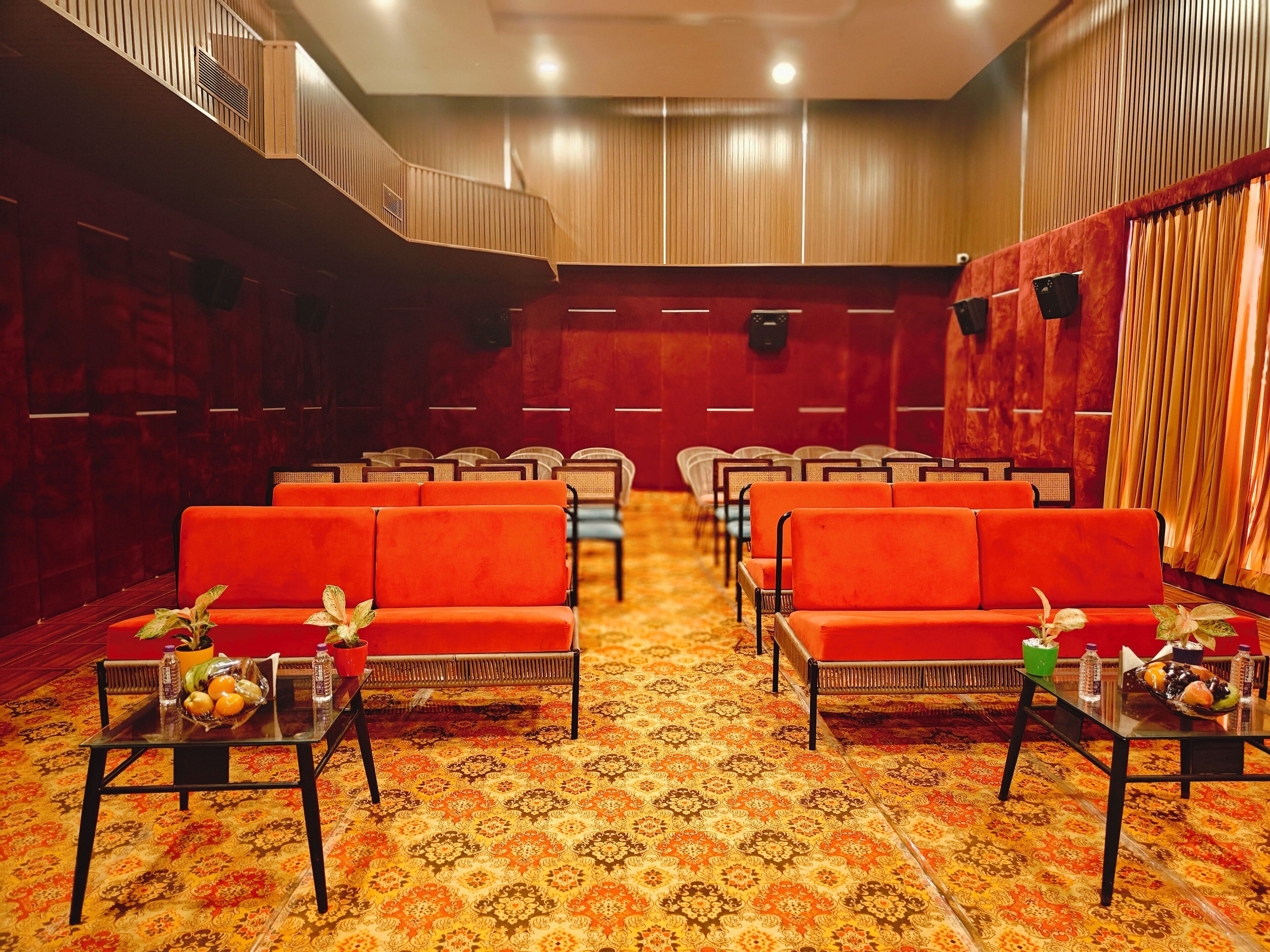 Una sala de conferencias con hileras de sofás naranja, una alfombra estampada y una pared de madera con listones verticales.