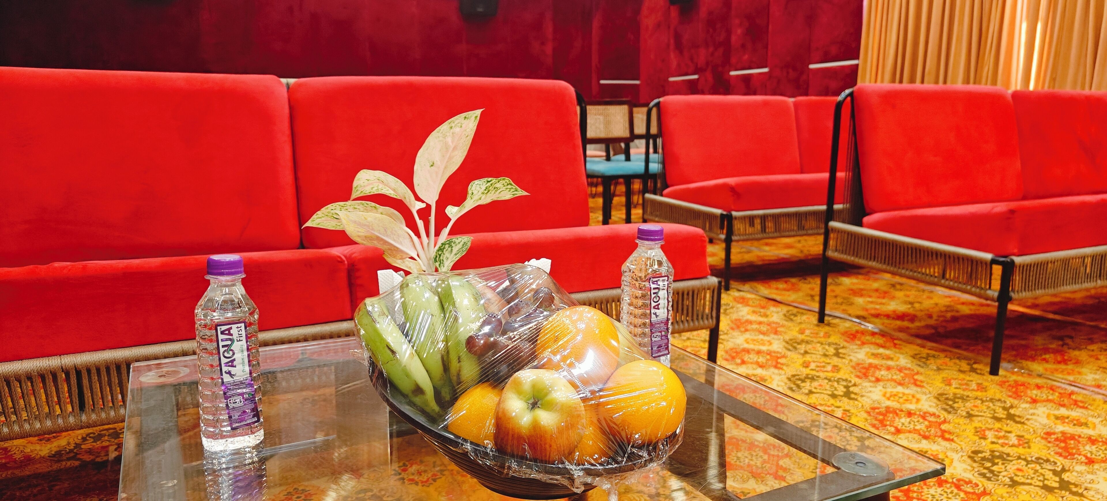 A room with red sofas, a glass table with fruit and water bottles, and a patterned carpet.